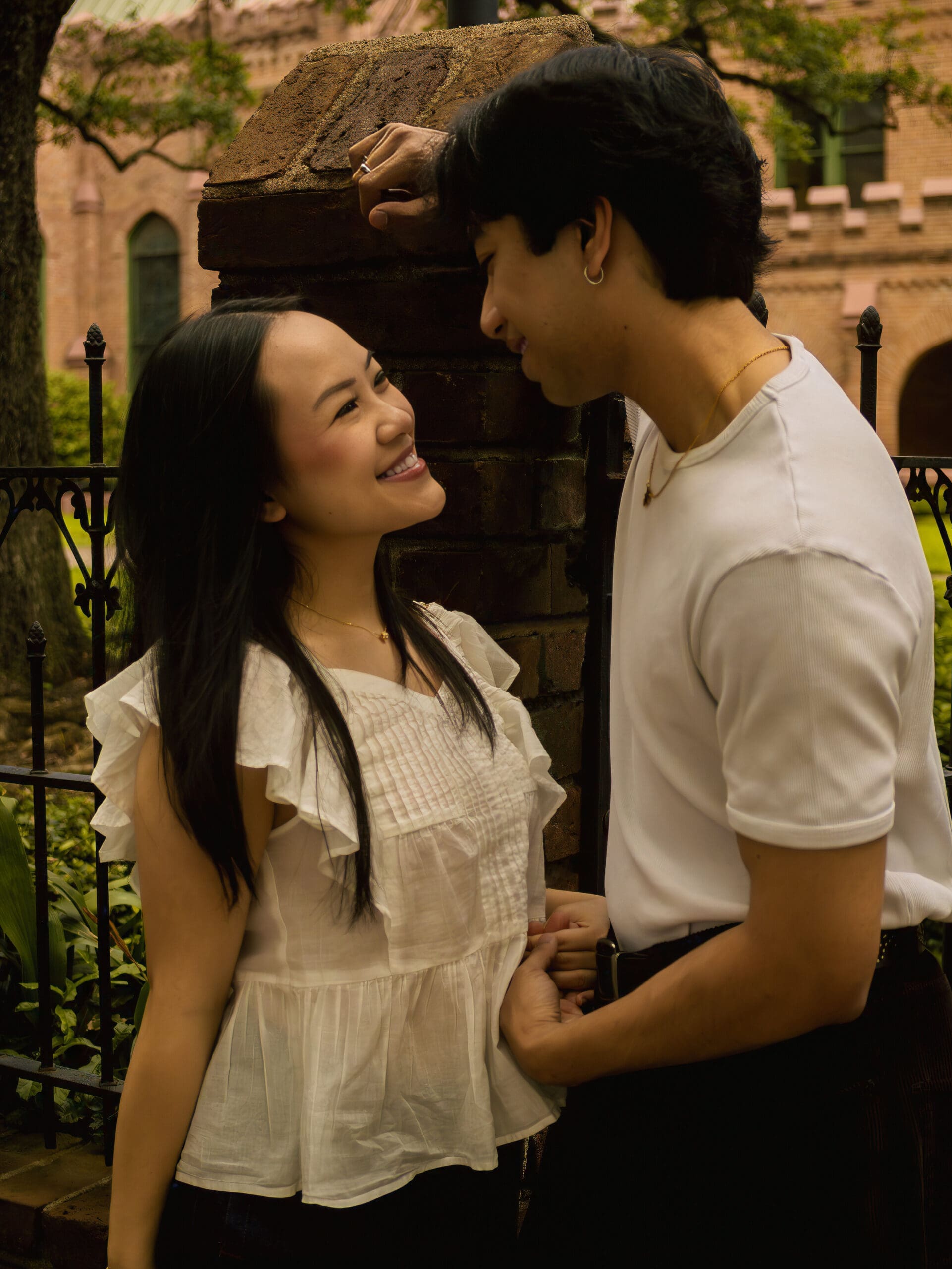 Couple smiling together during a downtown Houston engagement session near romantic brick architecture and garden greenery.
