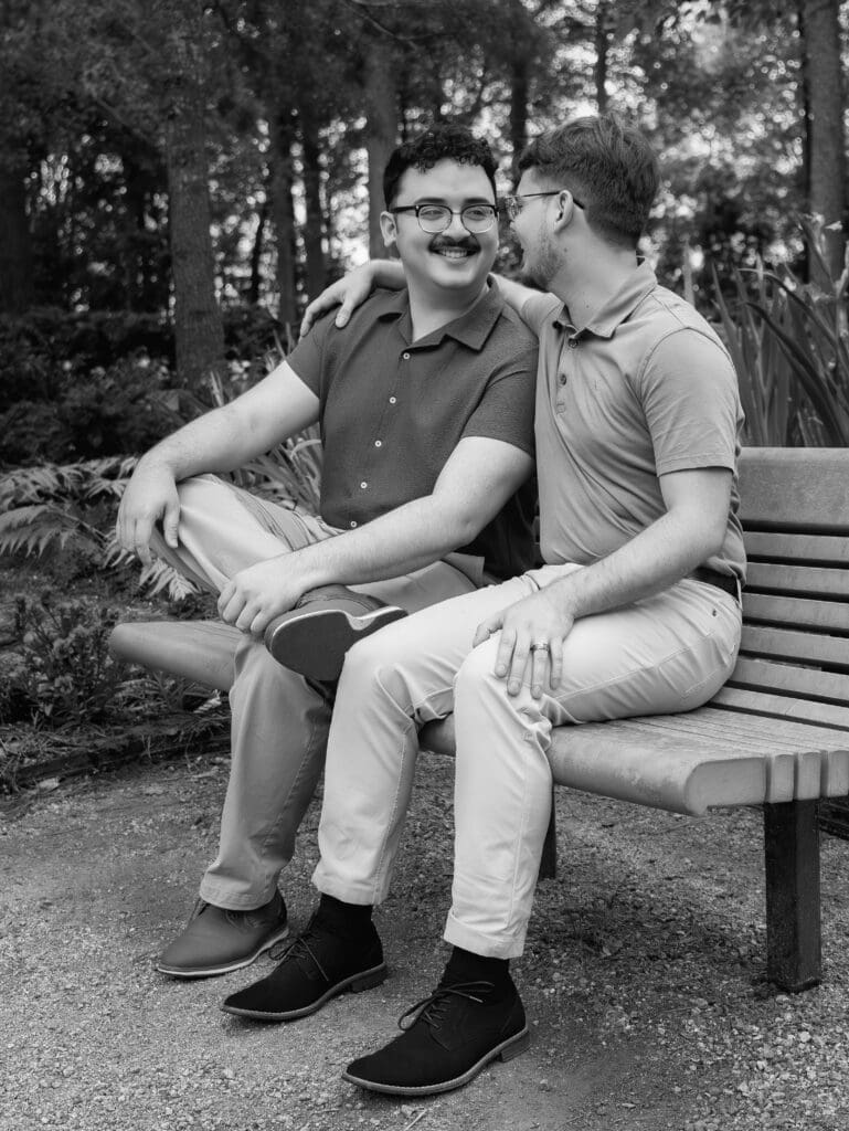 Engaged couple smiling at each other while seated on a bench at Mercer Botanic Gardens in Houston, Texas during a romantic garden engagement session.