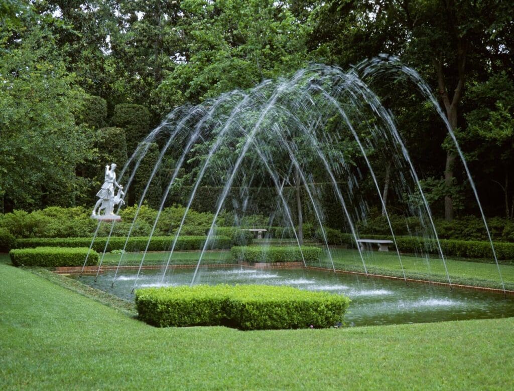 Arched fountain spraying over a formal garden pond at Bayou Bend Collection and Gardens in Houston, Texas.