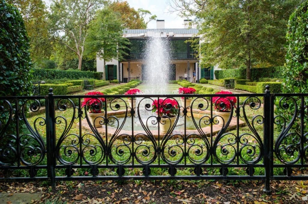 Formal fountain courtyard at Bayou Bend Collection and Gardens in Houston, Texas, featuring manicured hedges, wrought iron fencing, and historic estate architecture.